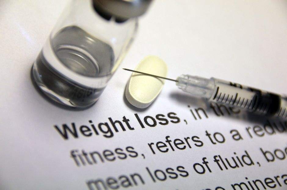 A syringe and a pill on top of a paper with the words weight loss on it