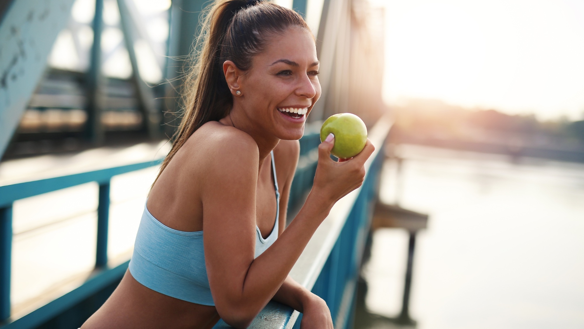 A woman eating an apple on a pedestrian bridge